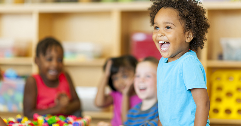 Young boy in blue shirt, smiling in classroom