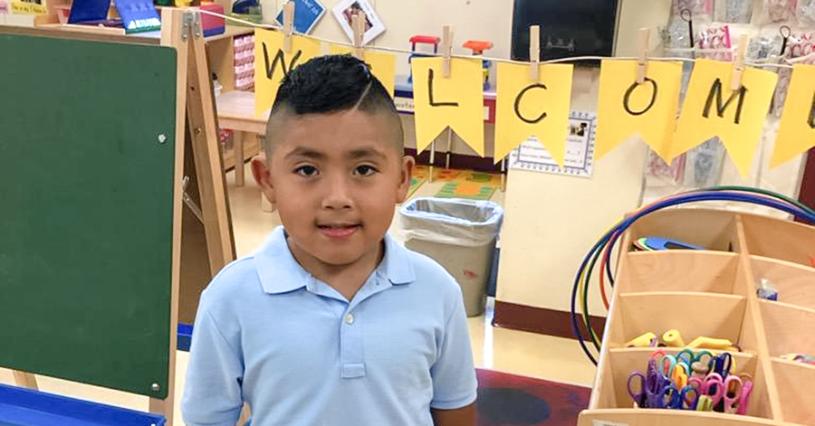 preschool boy with blue shirt standing in classroom