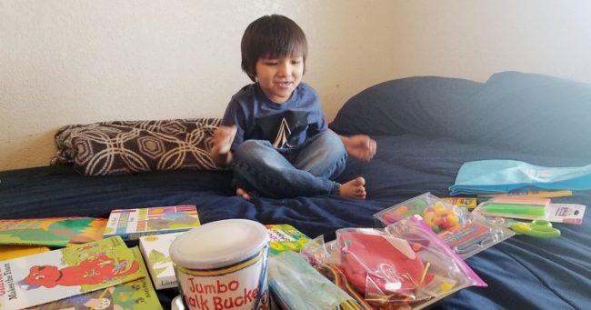 Young boy sitting on a bed surrounded by books and activities.