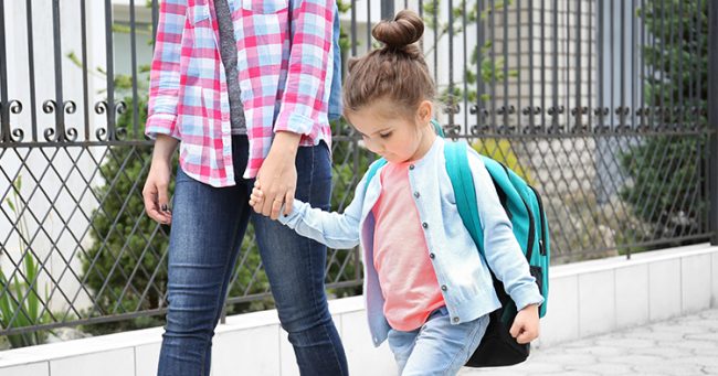 little girl with backpack holding hand of adult woman, walking outside