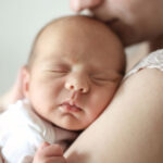 Woman holding newborn baby, who has their eyes closed.