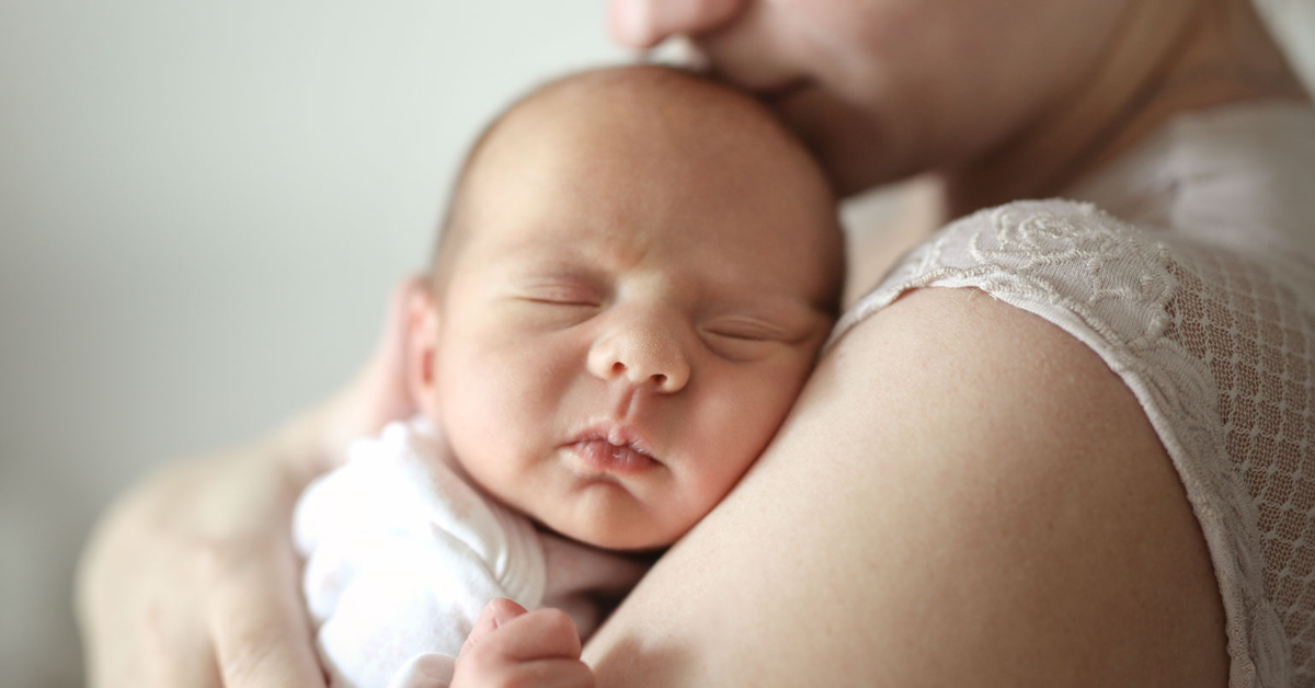 Woman holding newborn baby, who has their eyes closed.