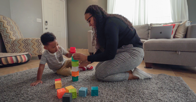 Mom kneeling down on floor playing blocks with son