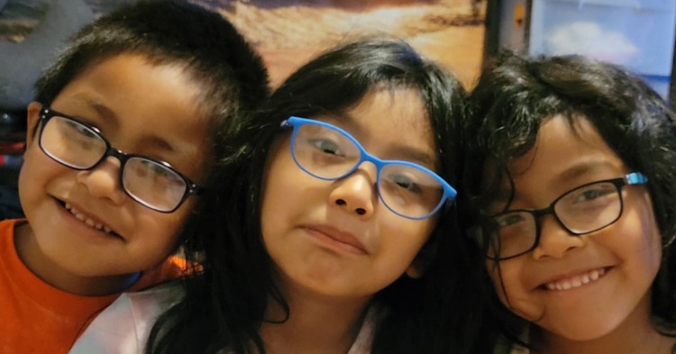 three kids smiling and wearing glasses