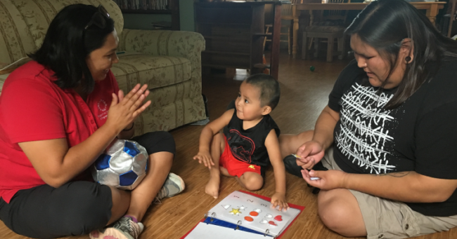 A home visitor works with the family and a small child in their home on a puzzle. Retaining home visitors.