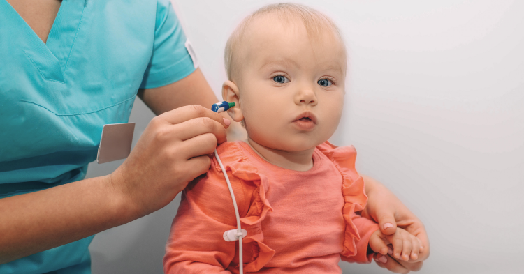 Baby in pink shirt getting hearing screening, developmental screenings