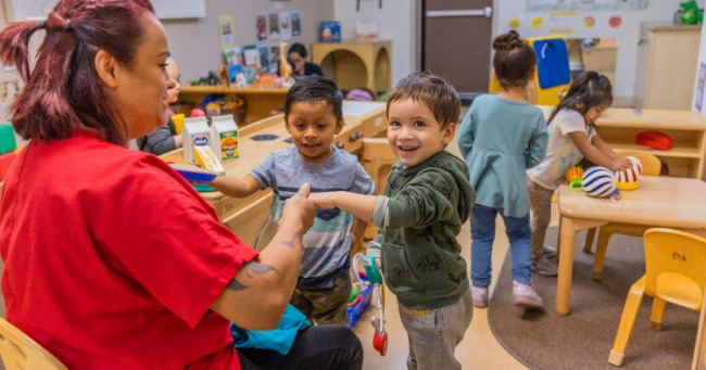 two little boys talking with child care provider in a classroom.