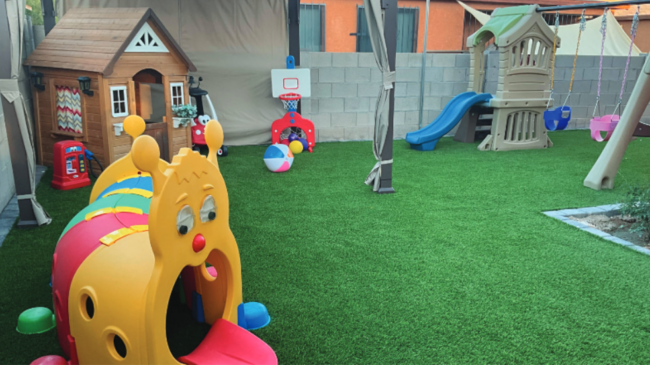 A backyard playground with a playhouse, artificial turf, slide and play tunnel.