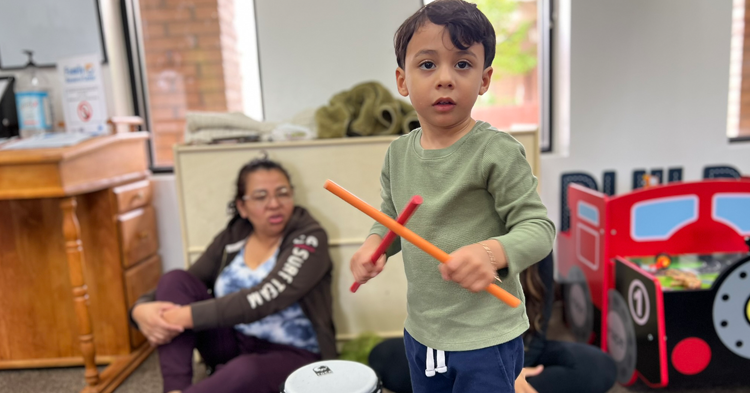 Young boy holding drum sticks and standing in front of a small bongo drum.