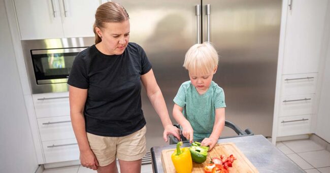 Mom in kitchen helping toddler son cut vegetables