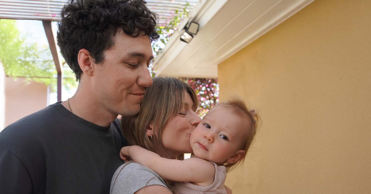 Mom and dad, embracing and kissing toddler girl