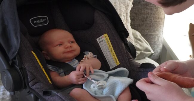Newborn in car seat interacting with his mother