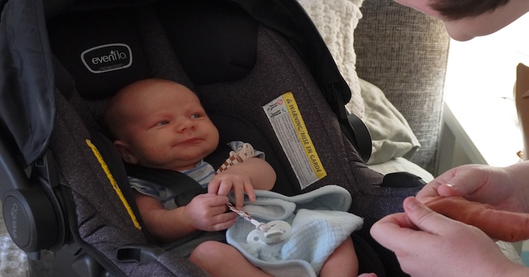 Newborn in car seat interacting with his mother