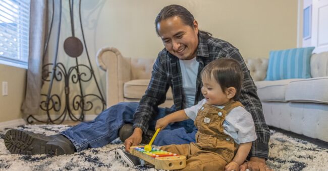 Father playing with a musical instrument next boy toddler